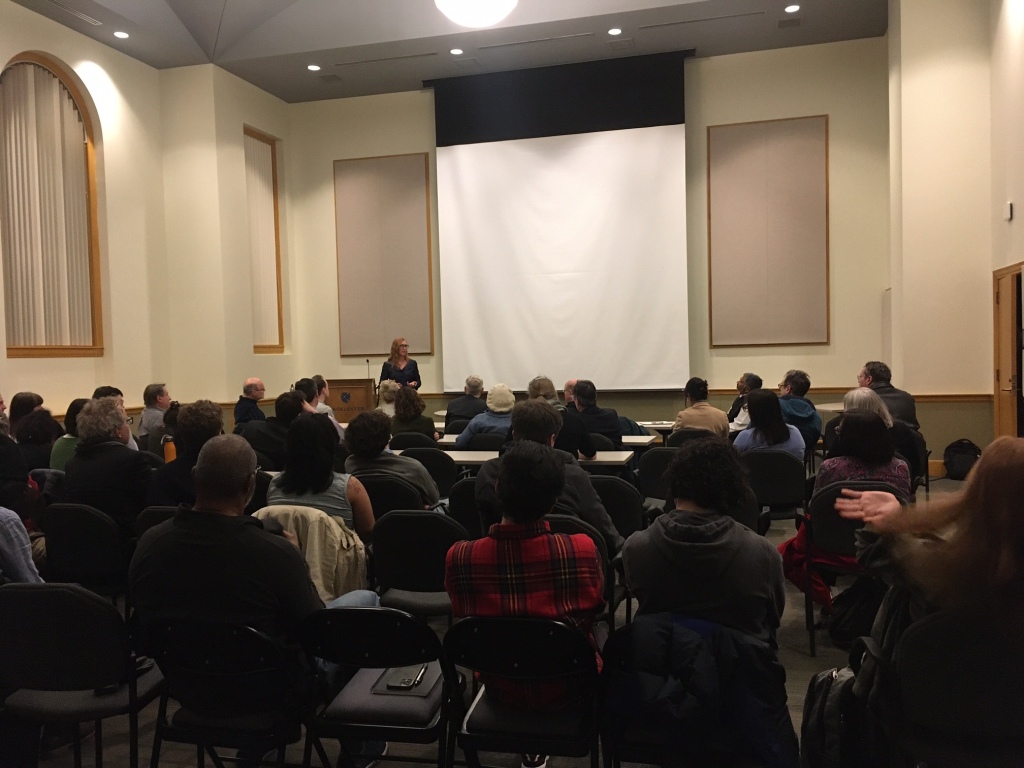 Picture of Dr. Julia Schleck lecturing to a full lecture hall of faculty, staff, students, and senior administrators, at Macalester College.